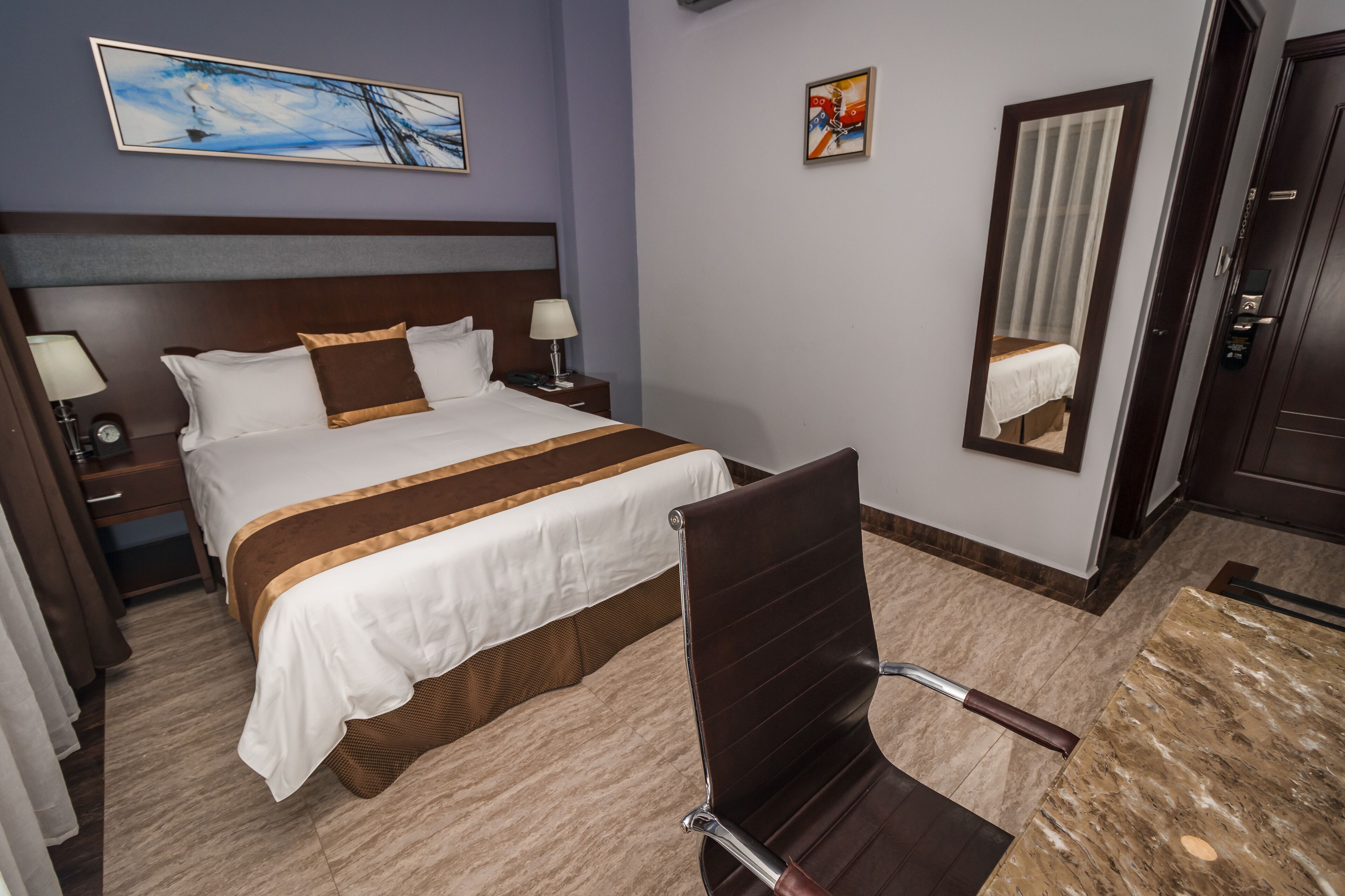 A hotel room with a large bed, a chair, a nightstand, a lamp, and a mirror.