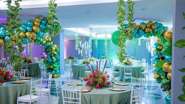 Une salle de banquet avec des tables rondes, des chaises blanches et des nappes vertes.