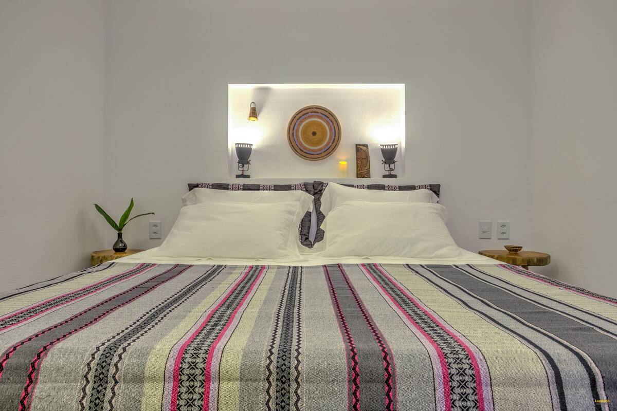 Un lit bien fait, recouvert d’une couverture à rayures, deux tables de chevet avec des lampes et un luminaire fixé au mur.