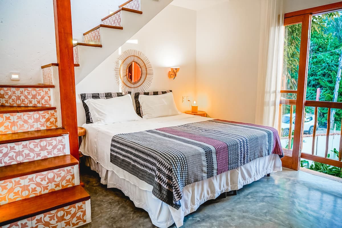 Une chambre à coucher comprenant un lit, une table de chevet, un miroir, un escalier et une vue sur l’extérieur.