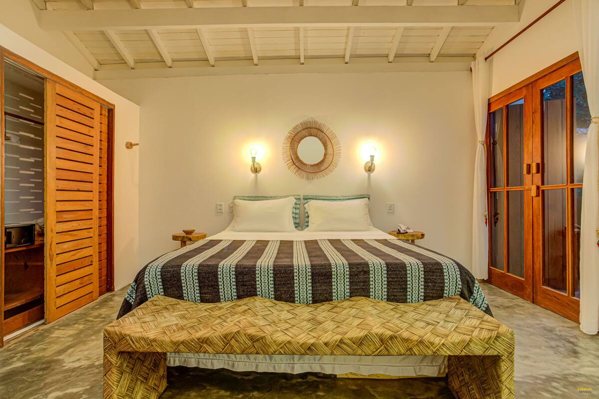 Une chambre à coucher comprenant un lit, des tables de chevet, un banc, un miroir et une armoire.