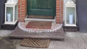 Una puerta verde con marco de ladrillo, flanqueada por dos macetas y dos faroles.