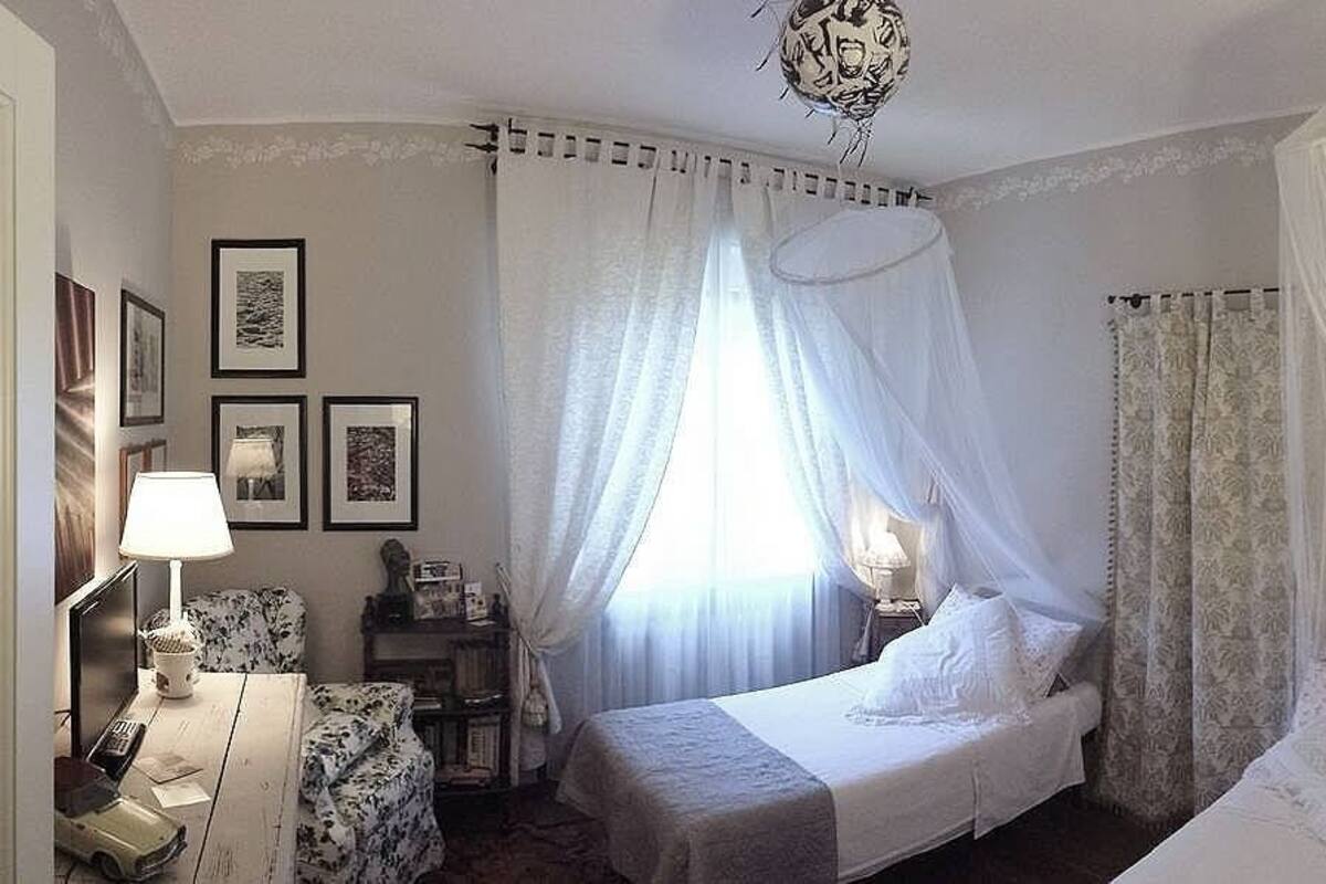 Hotellihuone, jossa on sänky, yöpöytälamput, tuoli, työpöytä ja ikkuna, jossa on verhot.