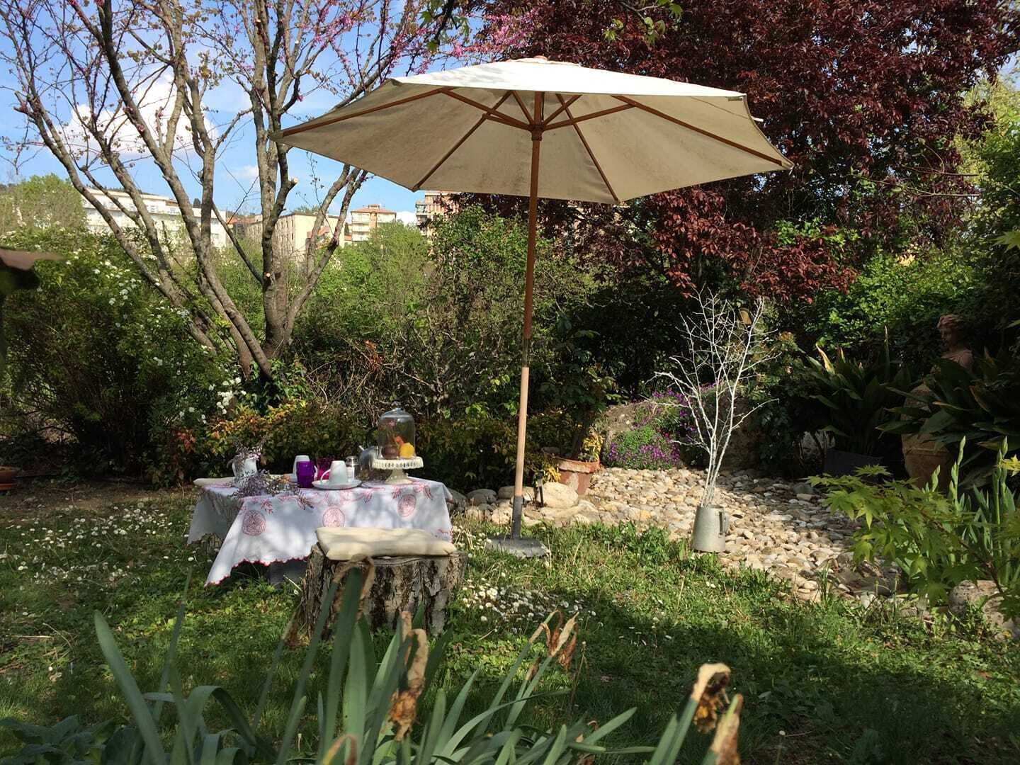 A garden setting with a table set for a meal, surrounded by various plants and a decorative tree stump.