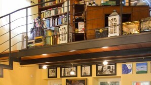 Un salón acogedor con un sofá rojo, una estantería llena de libros y objetos decorativos, y un cuadro grande en la pared.