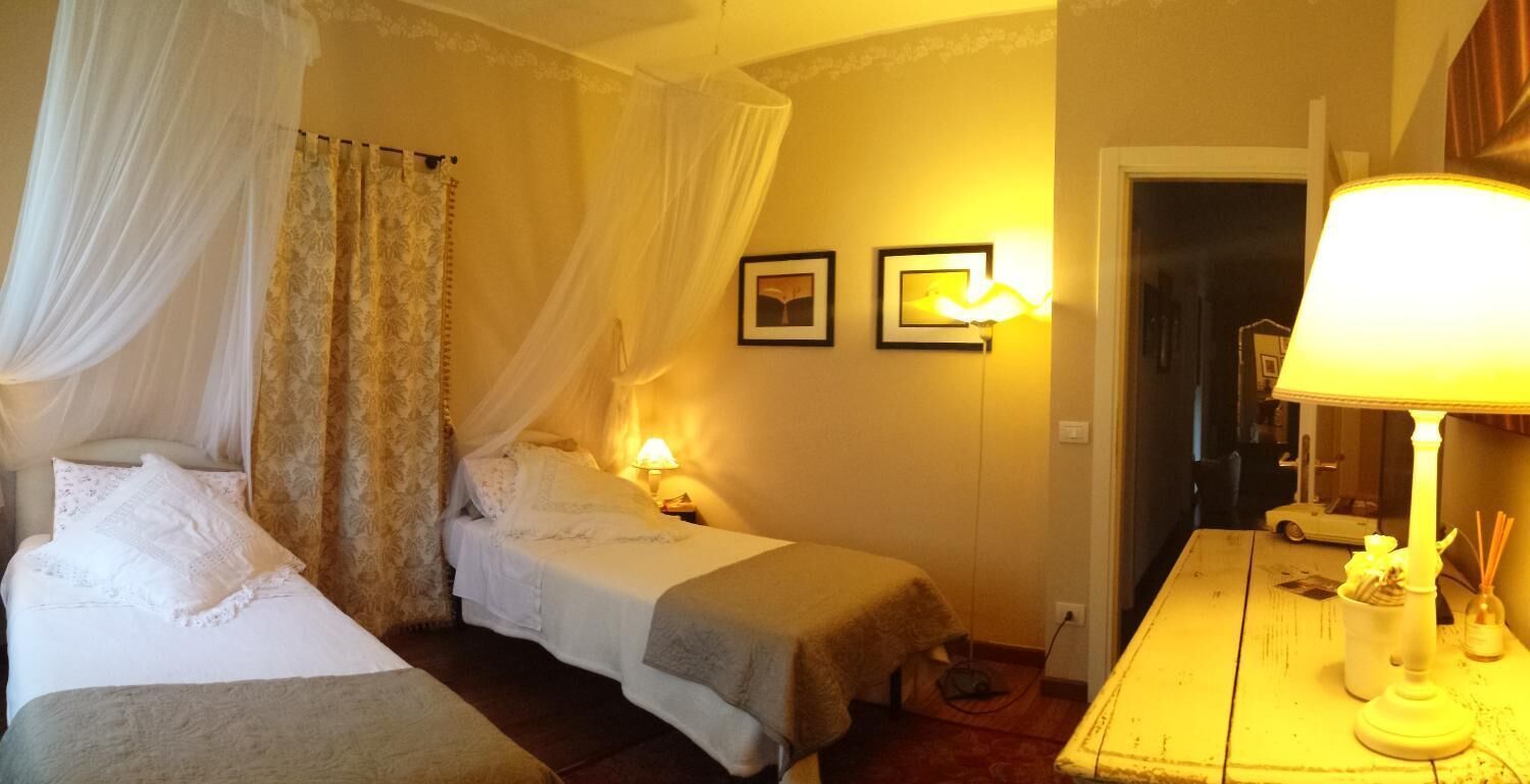 Ein Hotelzimmer mit zwei Betten, einem Baldachinbett, einem Nachttisch mit Lampe sowie einem kleinen Tisch mit Lampe und Kerzenhalter.
