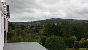 Vista de uma varanda sobre paisagem rural com colinas ondulantes, vegetação densa e uma aldeia ao longe.