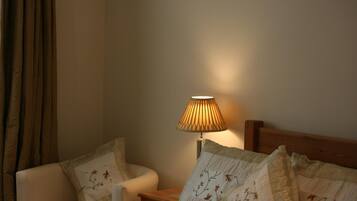 A cozy room with a bed, a nightstand, a lamp, and a chair.