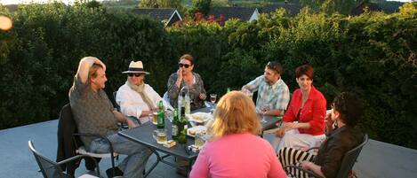 A group of people seated around a table outdoors, engaged in conversation.