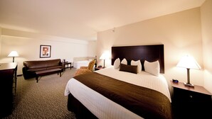 A hotel room with a large bed, a sofa, a desk, and two lamps. - Cobblestone Inn & Suites – Manchester (Manchester)