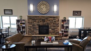 A cozy lobby with a stone fireplace, a large clock, and comfortable seating. - Cobblestone Inn & Suites – Manchester (Manchester)
