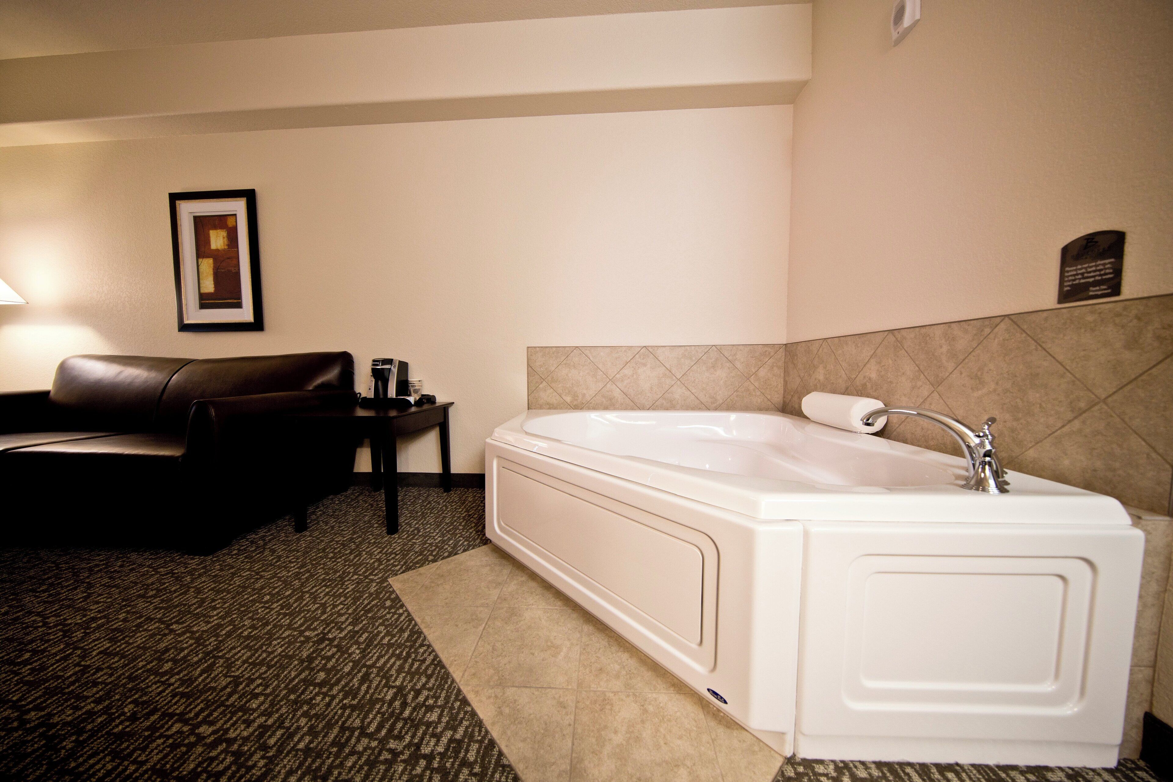 Un baño de hotel con una bañera grande, un sofá de cuero oscuro y una mesita con lámpara.