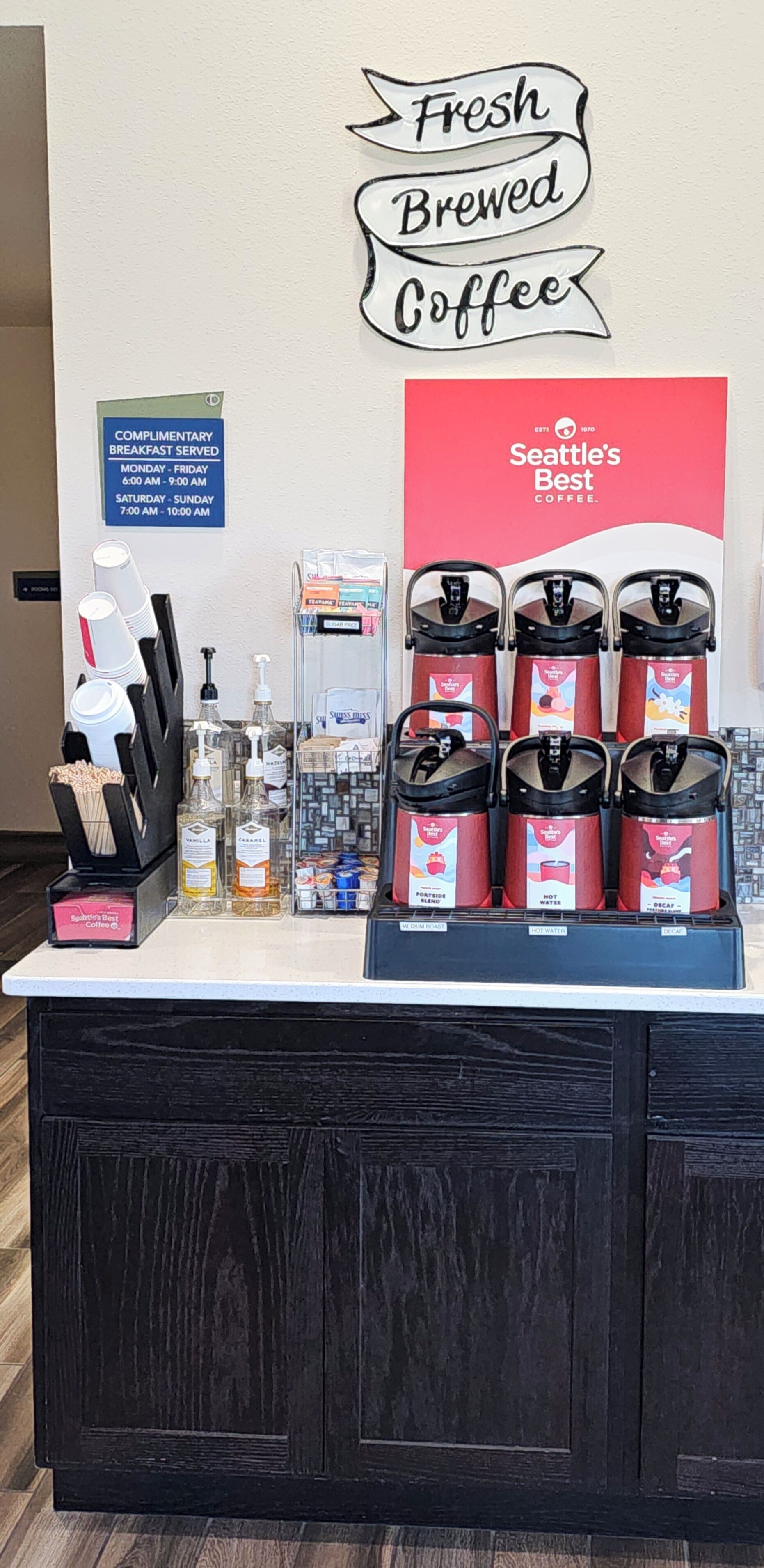 A coffee station with Seattle's Best branded coffee dispensers, a complimentary breakfast sign, and various coffee-making supplies.