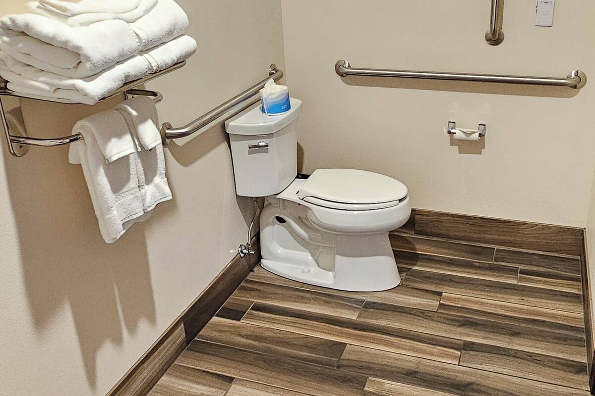 Une salle de bain équipée de toilettes, de barres d’appui et d’un porte-serviettes avec des serviettes pliées.