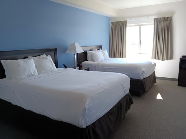 Una habitación de hotel con dos camas, una mesita de noche, una lámpara y un ventanal con cortinas.