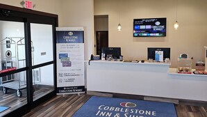 A hotel reception area with a Cobblestone Rewards sign, a computer, and a digital screen displaying hotel information. - Cobblestone Inn & Suites – Manchester (Manchester)