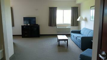 A living room with a flat-screen TV, a sofa, a coffee table, and a window with curtains.