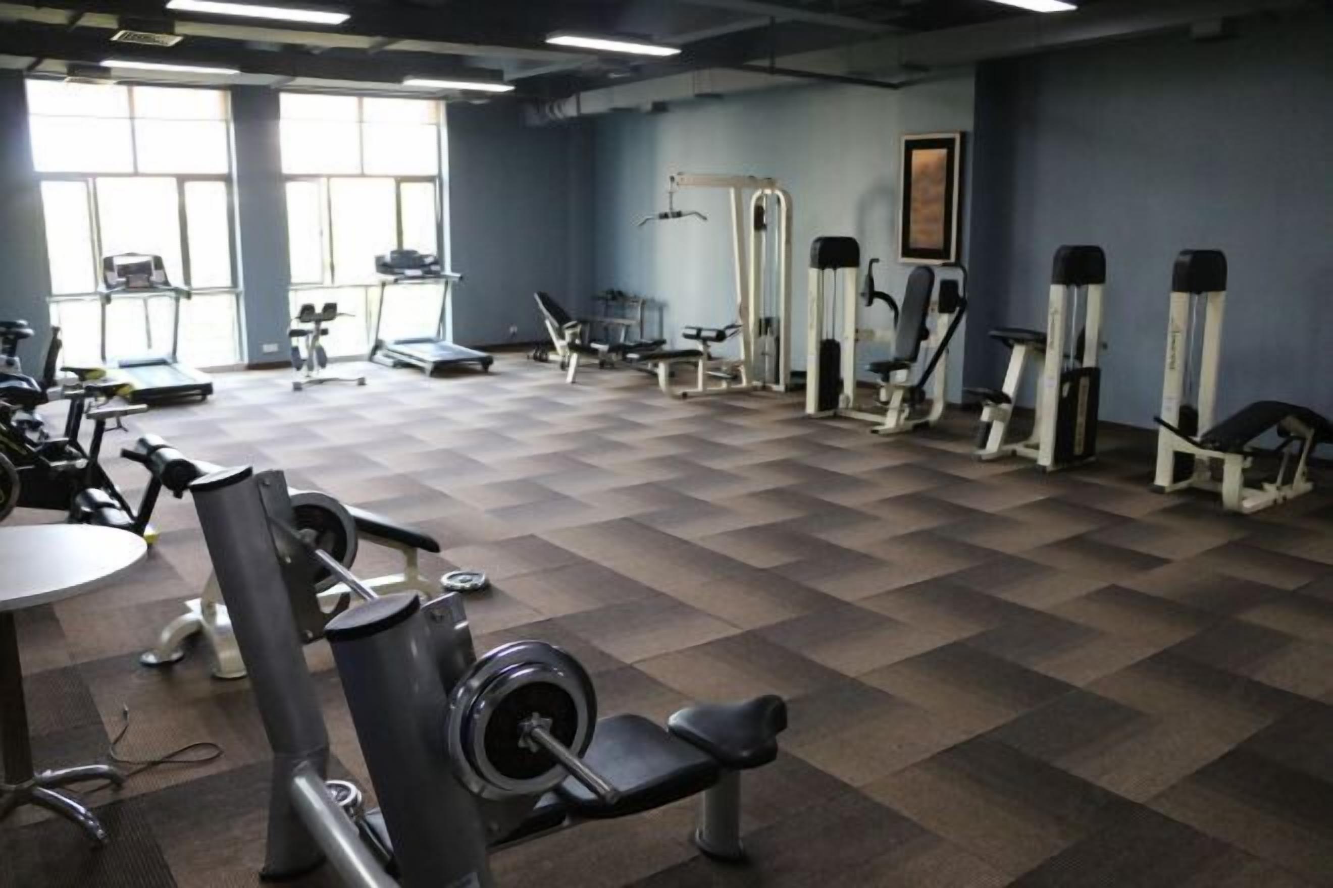 Un gimnasio con varios equipos de ejercicio, ventanas amplias y suelo a cuadros.