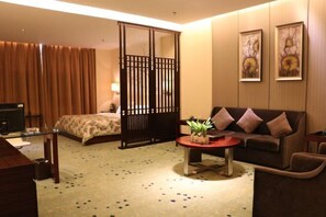 A hotel room with a bed, a sofa, a coffee table with a plant, a TV, and a sliding door. - Hetian Hotel (Wuhan)