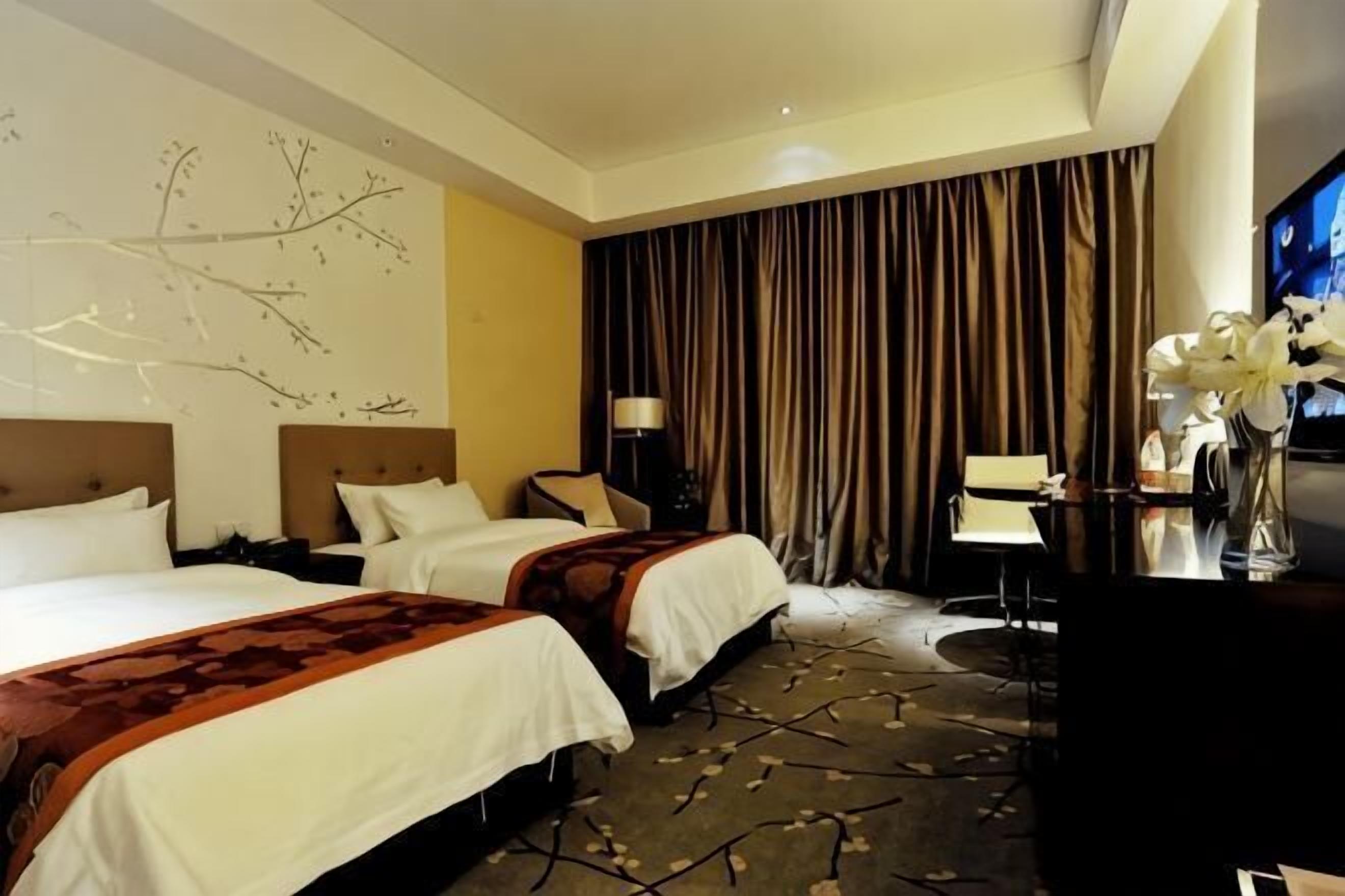 A hotel room with two beds, a desk, a chair, and a television.