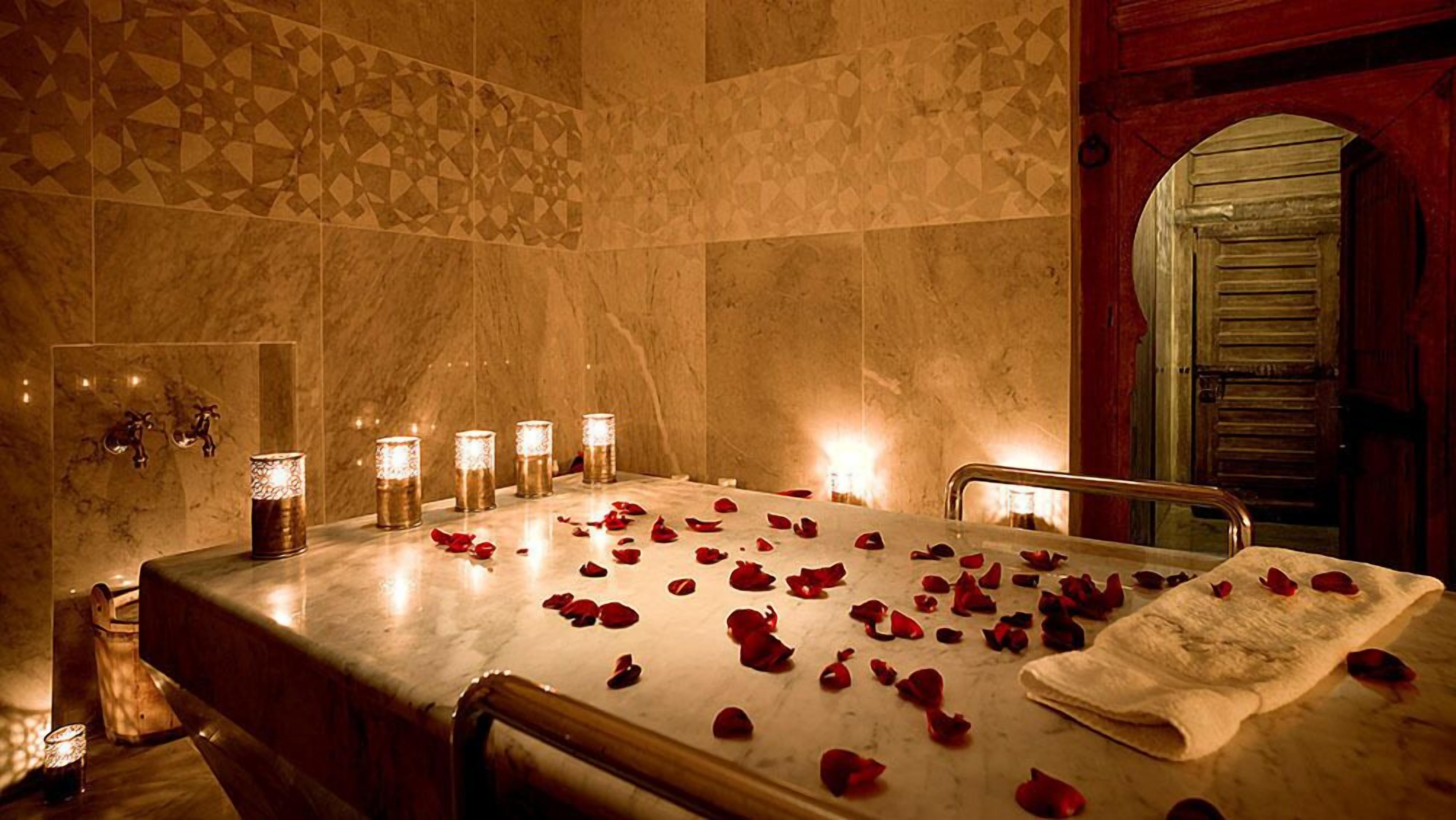 Un cuarto de spa con una bañera de mármol, pétalos de rosa, velas y una toalla sobre la mesa.
