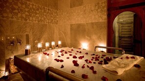 A spa room with a marble bath, rose petals, candles, and a towel on the table. - Monte Bianco (Astana)