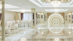 A spacious banquet hall with round tables and chairs, a central decorative light fixture, and a polished marble floor. - Monte Bianco (Astana)