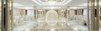 Un amplio salón de banquetes con mesas y sillas redondas, una lámpara decorativa en el centro y un suelo de mármol pulido.
