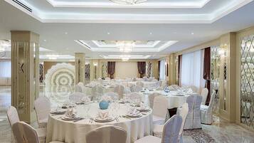 A banquet hall with round tables set for dining, elegant chandeliers, and a high ceiling.