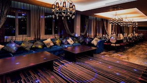 A modern lounge area with a long sofa, multiple tables, and elegant chandeliers. - Monte Bianco (Astana)