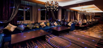 A modern lounge area with a long sofa, multiple tables, and elegant chandeliers.