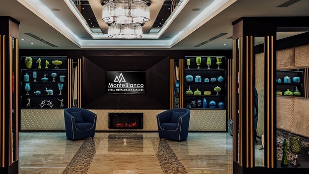 A modern interior with a fireplace, two blue armchairs, and shelves of decorative items. - Monte Bianco (Astana)