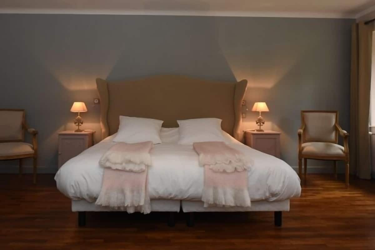 A large bed with a wooden headboard, two bedside tables with lamps, and two armchairs.