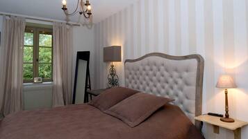 Un dormitorio con cabecera capitonada, lámpara de noche, espejo y ventana con cortinas.