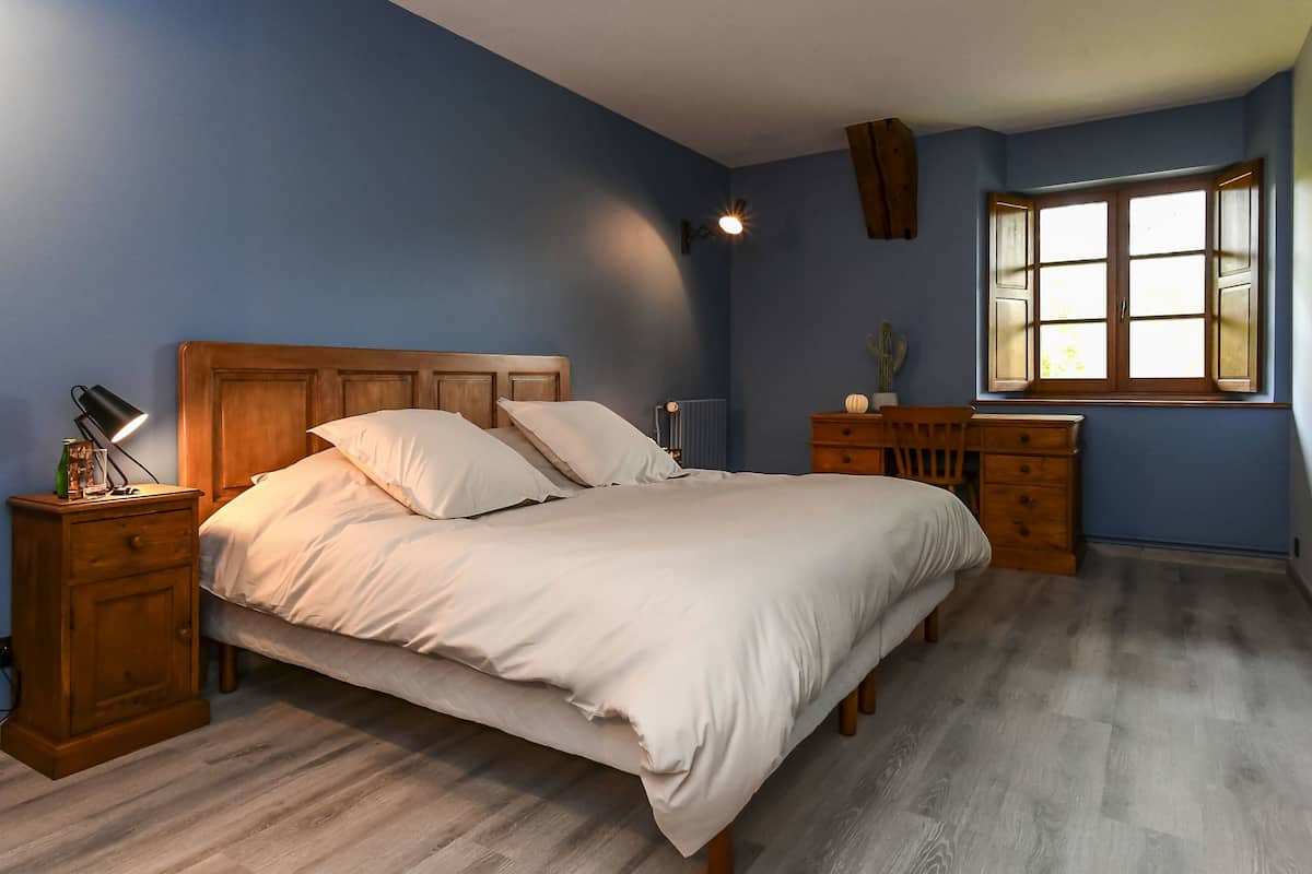 A bedroom with a wooden bed, a nightstand, a dresser, and a window with a view.