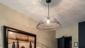 Een hal met een houten bankje, een hanglamp en een kunstwerk in een lijst aan de muur.