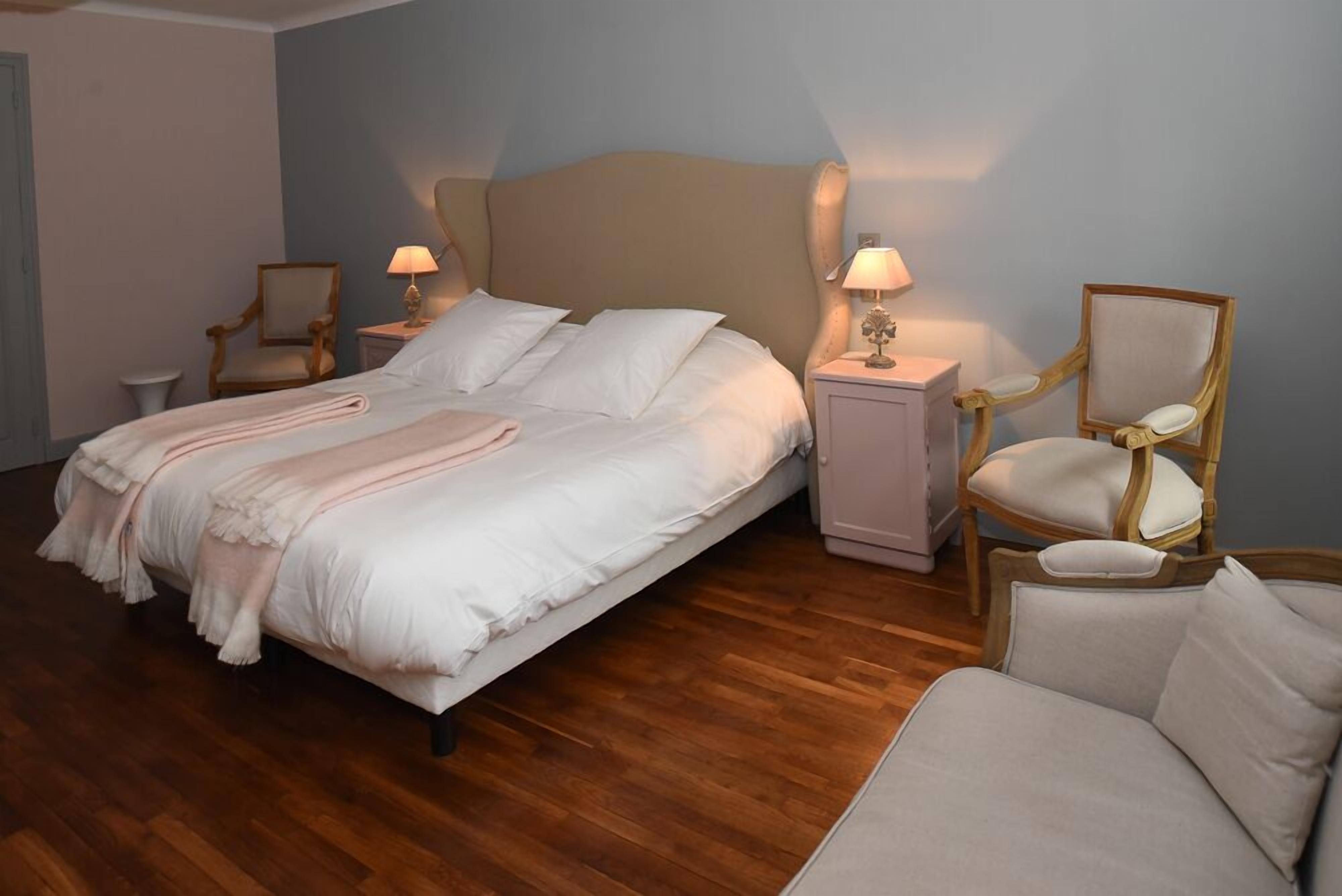 Un dormitorio con una cama, dos mesitas de noche, una silla y un sofá.