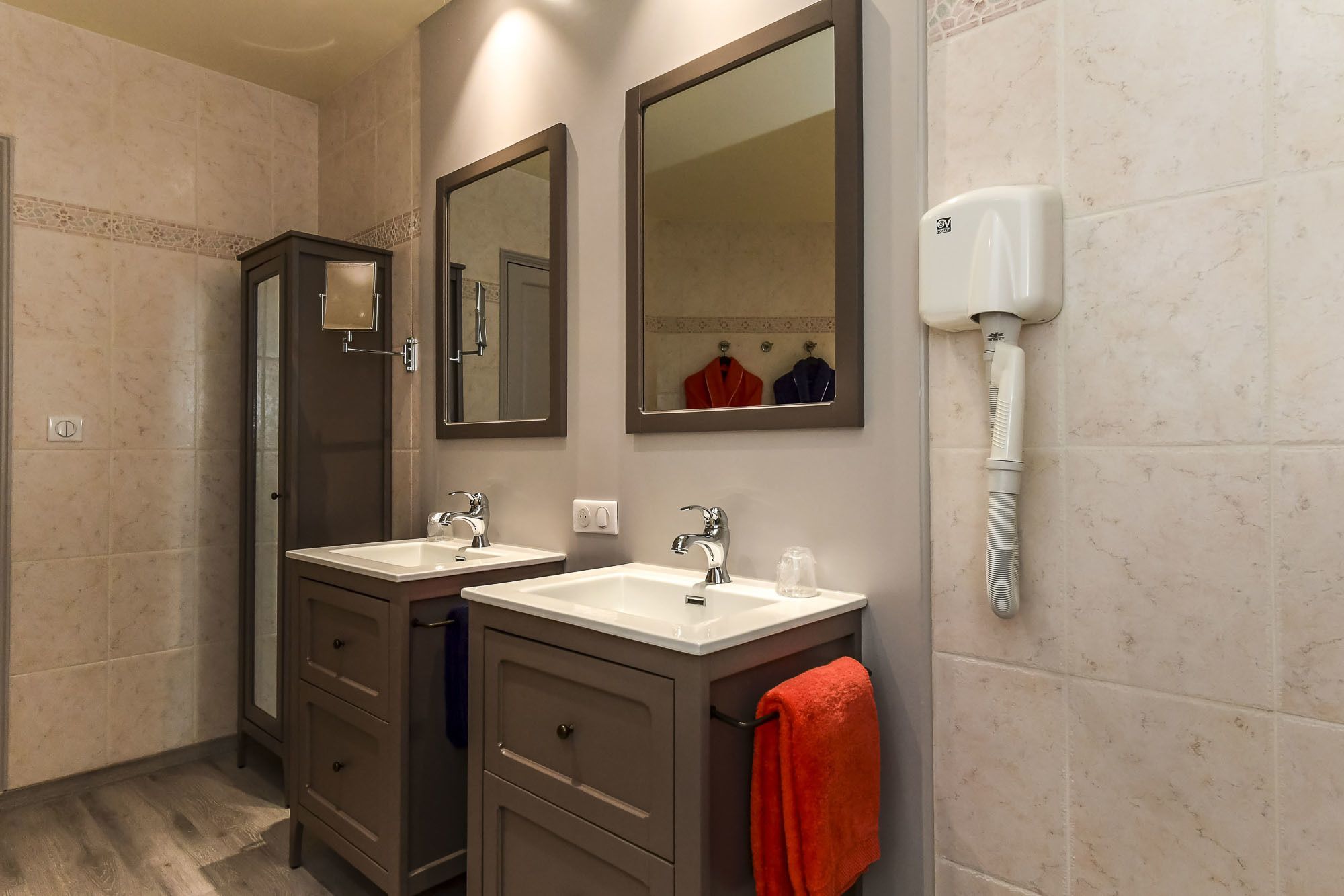A bathroom with two sinks, a mirror, a towel rack, and a hand dryer.