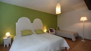 A bedroom with a large bed and a smaller bed, both with white headboards and green pillows. There are bedside lamps on nightstands, and a floor lamp in the corner.