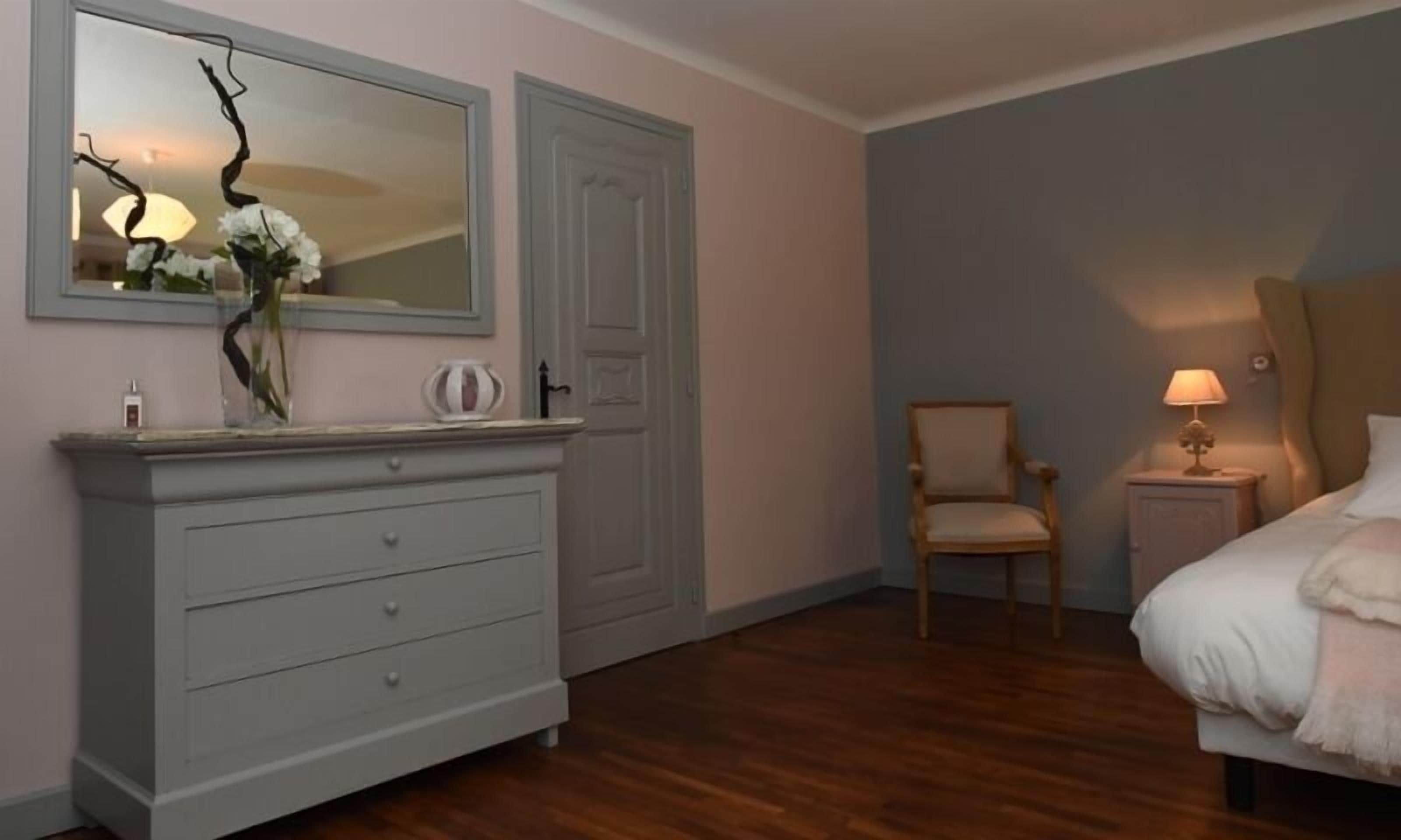 A bedroom with a bed, a nightstand, a chair, a dresser, and a mirror.