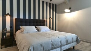Een keurig opgeruimde slaapkamer met een groot bed, een gestreepte wand en twee bedlampen.