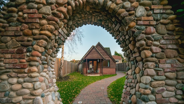 A stone archway leading to a house with a brick exterior and a small porch. - Brook Barn with Sauna & Hot Tub (St Neots)