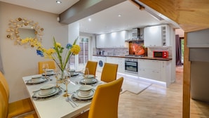 A modern kitchen with white cabinets, a red microwave, and a wooden staircase. - Brook Barn with Sauna & Hot Tub (St Neots)