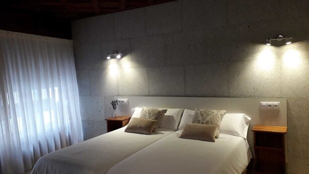 A bedroom with a large bed, two bedside tables, and a wall-mounted light fixture. - Hostal Vendaval (Ortigueira)