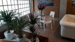 A modern interior with a glass table, white chairs, a white sofa, and potted plants. - Hostal Vendaval (Ortigueira)