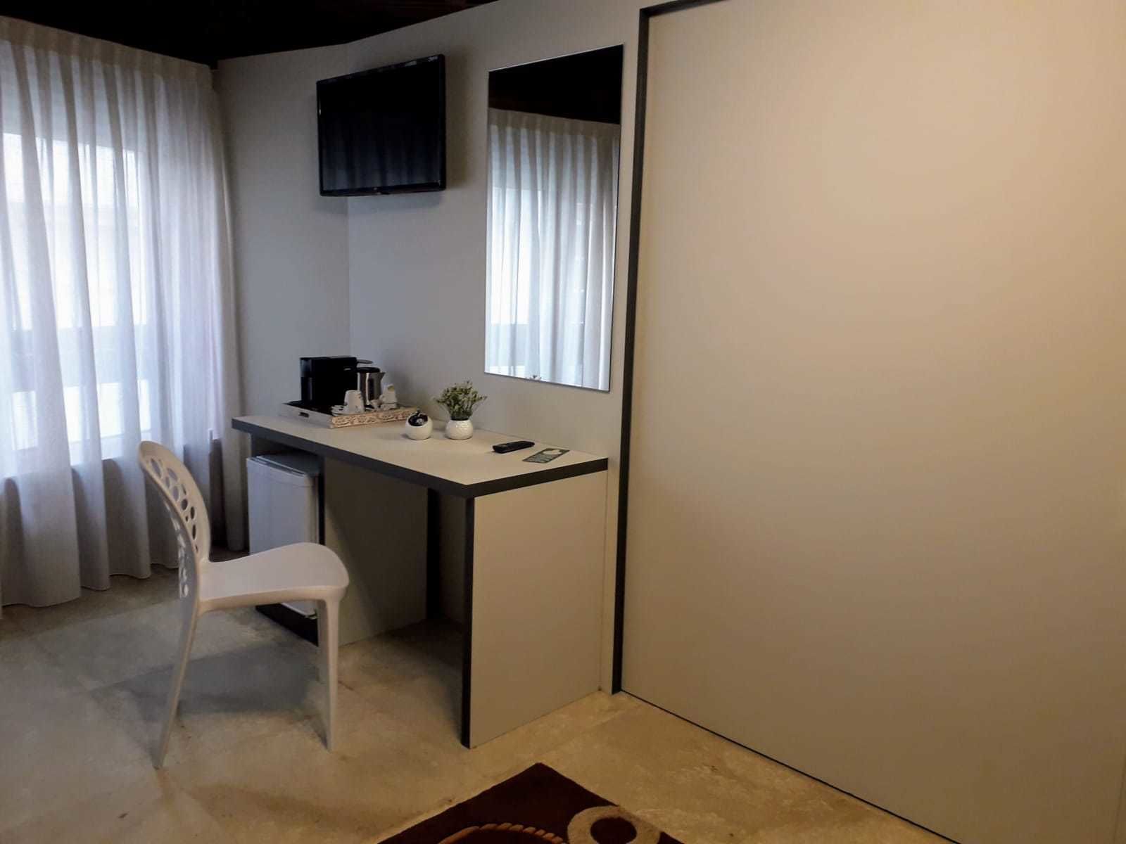 A small, neatly arranged room with a desk, chair, and a television mounted on the wall.