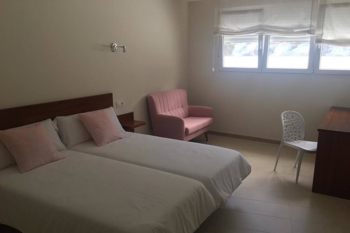 A bedroom with two beds, a desk, a chair, and a window with curtains.