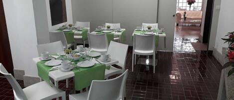 A dining area with white tables and chairs, green tablecloths, and a tiled floor.
