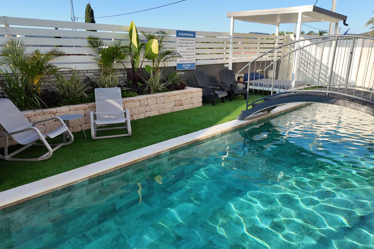 A swimming pool with clear water, surrounded by artificial grass, and equipped with lounge chairs.