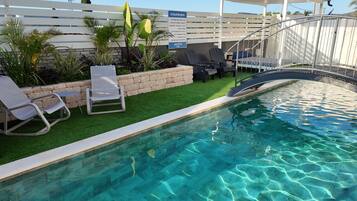 A swimming pool with clear water, surrounded by artificial grass, and equipped with lounge chairs.